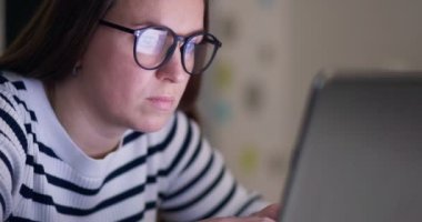 A focused woman in glasses looking at laptop screen with using internet, reading, watching, typing, working online. High quality 4k footage