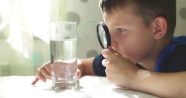 Çocuk büyüteçle bardaktaki suya bakıyor. Su kalite kontrol konsepti. Yüksek kalite 4k görüntü