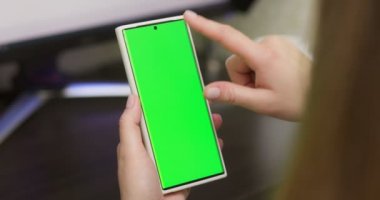 Woman using smartphone in vertical mode with green mock-up screen, doing swiping, scrolling gestures. Internet social networks browsing news, financial reports. High quality 4k footage