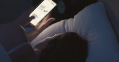 Bir kadın gece yatağa uzanıyor ve akıllı telefon kullanıyor. Cep telefonu kullanan, sosyal medyada gezinen, sohbet eden, flört uygulamaları kullanan, yatmadan önce internet alışverişi yapan bir kadın. Yüksek kalite 4k görüntü