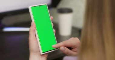Kadın dikey modda akıllı telefon kullanıyor, yeşil ekran maketi kullanıyor, kaydırma hareketleri yapıyor. İnternet sosyal ağları, internet haberleri, finansal raporlar. Yüksek kalite 4k görüntü