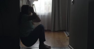 Silhouette of a sad woman sliding down the wall of her apartment, covering face with hands. Getting bad news, eviction, depression, trouble , death in the family. High quality 4k footage