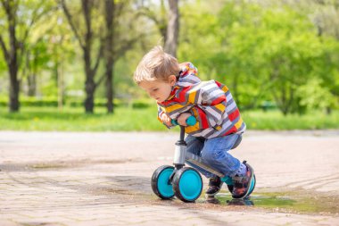 Active blond boy riding balance bike or run bike outdoor park. Active kid playing outside