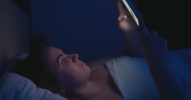 Bir kadın gece yatağa uzanıyor ve akıllı telefon kullanıyor. Cep telefonu kullanan, sosyal medyada gezinen, sohbet eden, flört uygulamaları kullanan, yatmadan önce internet alışverişi yapan bir kadın. Yüksek kalite 4k görüntü