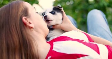 Woman lying on a lawn in the garden and playing with husky puppy dog. High quality 4k footage