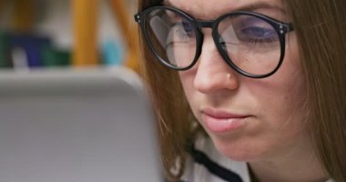 A focused woman in glasses looking at laptop screen with using internet, reading, watching, typing, working online. High quality 4k footage