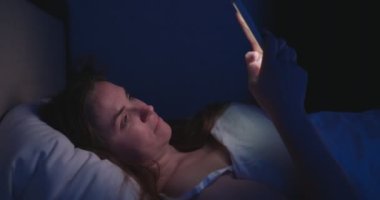 Bir kadın gece yatağa uzanıyor ve akıllı telefon kullanıyor. Cep telefonu kullanan, sosyal medyada gezinen, sohbet eden, flört uygulamaları kullanan, yatmadan önce internet alışverişi yapan bir kadın. Yüksek kalite 4k görüntü