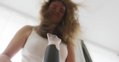 Beautiful young woman using hair dryer near the window at home. High quality 4k footage