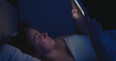 Bir kadın gece yatağa uzanıyor ve akıllı telefon kullanıyor. Cep telefonu kullanan, sosyal medyada gezinen, sohbet eden, flört uygulamaları kullanan, yatmadan önce internet alışverişi yapan bir kadın. Yüksek kalite 4k görüntü