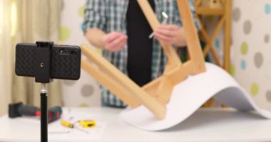 Handyman blogger shows assembling chair, shooting video instructions on smartphone . Man assembling furniture by yourself. Blog about carpentry. High quality 4k footage