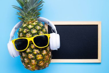 Güneş gözlüklü ananas ve mavi arkaplandaki mesajın için boş fotokopi tahtası olan kulaklık. Yaz tatili parti konsepti.