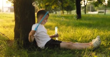 Child boy blows soap bubbles, having fun playing in park in rays of sunset. Child plays with soap bubbles in the summer garden. Happy childhood concept. High quality 4k footage