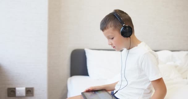 Niño Con Una Camiseta Blanca Usando Una Tableta Con Auriculares — Vídeo de stock