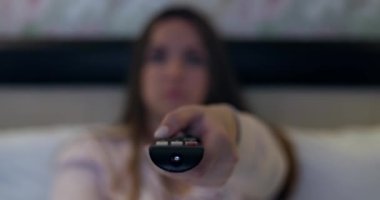 Elinde uzaktan kumanda tutan kadın televizyondaki kanalları değiştiriyor. Uzaktan kumandanın tuşlarına basıyor. Yüksek kalite 4k görüntü