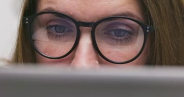 Close up view of focused woman in glasses looking at laptop screen with using internet, reading, watching, typing, working online. High quality 4k footage