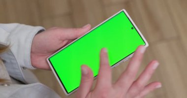 Woman with green screen chroma key smartphone scrolling through social media or online shop - internet, communications concept close up. High quality 4k footage