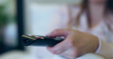 Elinde uzaktan kumanda tutan kadın televizyondaki kanalları değiştiriyor. Uzaktan kumandanın tuşlarına basıyor. Yüksek kalite 4k görüntü