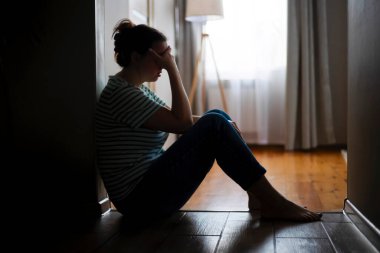 Evde yerde oturan üzgün ve depresif bir kadının silueti. Kötü haber, tahliye, depresyon, sorun, ailede ölüm.