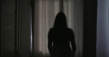 Güzel, genç esmer kadın, sabah güneşinin rahat dairesini aydınlatması için perdeleri açıyor. Kadın perdeleri açıyor ve gün ışığının tadını çıkarıyor. Yüksek kalite 4k görüntü