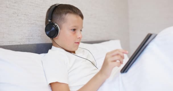 Chlapec Bílém Tričku Který Používá Tablet Sluchátky Sedí Doma Posteli — Stock video