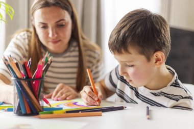 Anne ve çocuk evde masada oturan kalemlerle resim çiziyor. Mutlu aile