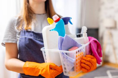 Elinde sepet dolusu temizlik malzemesi olan lastik eldivenli bir kadın evini temizlemeye hazır. Ev hanımlarının ev işleri, ev işleri ve profesyonel temizlik hizmetleri vardır. Alçak alan derinliği