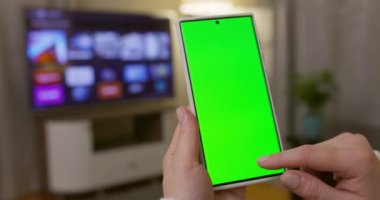 Dikey pozisyonda yeşil ekranlı akıllı telefonu tutan kadın ellerine yakın çekim. Yeşil modelli telefon kullanmak, internette sörf yapmak içerik videoları izlemek, uygulamalar. Yüksek kalite 4k görüntü