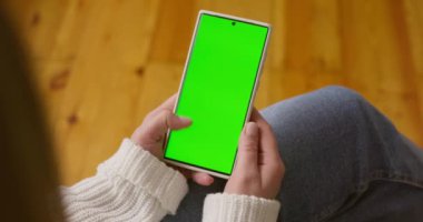 Dikey pozisyonda yeşil ekranlı akıllı telefonu tutan kadın ellerine yakın çekim. Yeşil modelli telefon kullanmak, internette sörf yapmak içerik videoları izlemek, uygulamalar. Yüksek kalite 4k görüntü