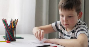 Bir çocuk masada otururken renkli kalemlerle beyaz kağıda resim çizer. Yüksek kalite 4k görüntü
