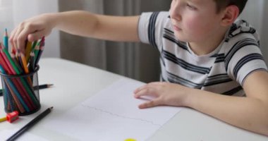 Bir çocuk masada otururken renkli kalemlerle beyaz kağıda resim çizer. Yüksek kalite 4k görüntü