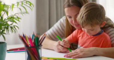 Anne ve çocuk evde masada oturan kalemlerle resim çiziyor. Mutlu bir aile. Yüksek kalite 4k görüntü