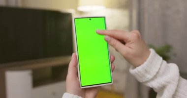 Dikey pozisyonda yeşil ekranlı akıllı telefonu tutan kadın ellerine yakın çekim. Yeşil modelli telefon kullanmak, internette sörf yapmak içerik videoları izlemek, uygulamalar. Yüksek kalite 4k görüntü