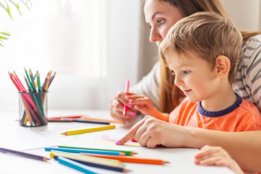 Anne ve çocuk evde masada oturan kalemlerle resim çiziyor. Mutlu aile