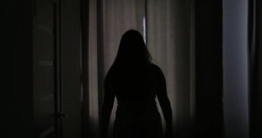 Güzel, genç esmer kadın, sabah güneşinin rahat dairesini aydınlatması için perdeleri açıyor. Kadın perdeleri açıyor ve gün ışığının tadını çıkarıyor. Yüksek kalite 4k görüntü