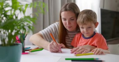 Anne ve çocuk evde masada oturan kalemlerle resim çiziyor. Mutlu bir aile. Yüksek kalite 4k görüntü