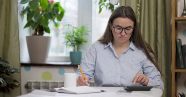 女性は家庭で国内の請求書を計算するために計算機を使用して 税金を支払うための書類を行う 高品質4K映像 — ストック動画