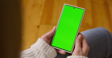 Dikey pozisyonda yeşil ekranlı akıllı telefonu tutan kadın ellerine yakın çekim. Yeşil modelli telefon kullanmak, internette sörf yapmak içerik videoları izlemek, uygulamalar. Yüksek kalite 4k görüntü