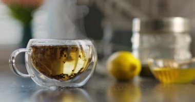 Yakın plan sıcak çay fincanı. Mutfaktaki ahşap masada dumanlı cam bardakta sıcak çay. Sıcak çay içeceği konsepti. Yüksek kalite 4k görüntü