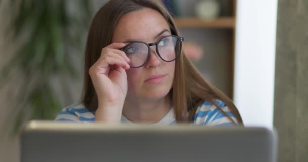 一个戴着眼镜 在笔记本电脑上工作的深思熟虑的女人 她把目光投向别处 思考着解决家里办公室问题的办法 做决定 觉得自己缺乏创意 闭目养神 — 图库视频影像