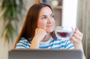 Masada oturmuş dizüstü bilgisayarla uğraşan gülümseyen bir kadın..
