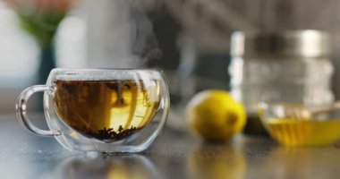 Yakın plan sıcak çay fincanı. Mutfaktaki ahşap masada dumanlı cam bardakta sıcak çay. Sıcak çay içeceği konsepti. Yüksek kalite 4k görüntü