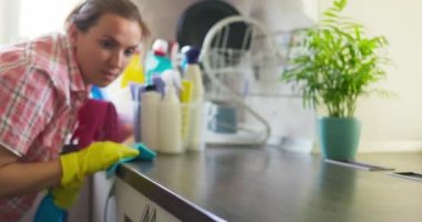 Sarı lastik eldivenli bir ev hanımı, mutfaktaki ahşap masa yüzeyini bir bez ve deterjanla siliyor, evi düzenli tutuyor. Yüksek kalite 4k görüntü