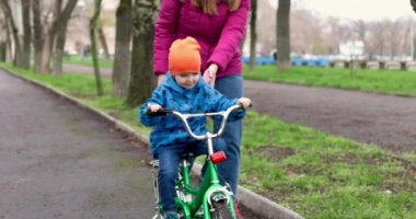 Anne oğluna bisiklet sürmeyi öğretiyor. Genç anne oğluna ilk kez parkta bisiklet sürmeyi öğretiyor. Bisikletli mutlu çocuklar. Birlikte geçirdiğimiz en güzel anlar. Çocukluk bisikleti konsepti. Yüksek kalite 4k görüntü