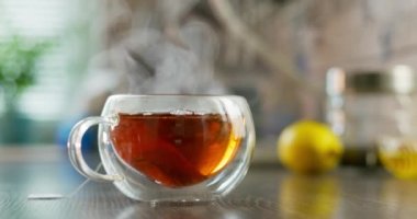 Yakın plan sıcak çay fincanı. Mutfaktaki ahşap masada dumanlı cam bardakta sıcak çay. Sıcak çay içeceği konsepti. Yüksek kalite 4k görüntü