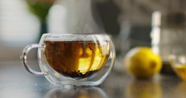 Yakın plan sıcak çay fincanı. Mutfaktaki ahşap masada dumanlı cam bardakta sıcak çay. Sıcak çay içeceği konsepti. Yüksek kalite 4k görüntü