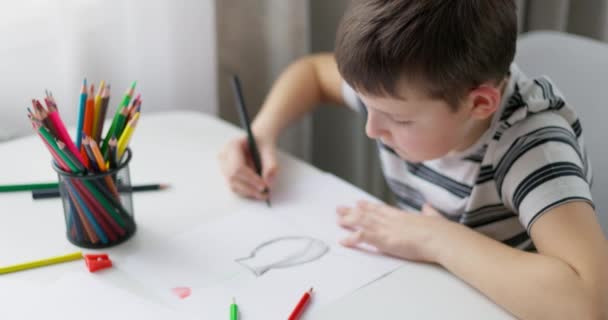 Een Jongetje Tekent Wit Papier Met Kleurpotloden Terwijl Hij Aan — Stockvideo