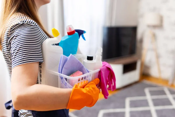 Woman in rubber gloves with basket of cleaning supplies ready to clean up her apartment. Housewife has many household chores, domestic work and professional cleaning service. Low depth of field