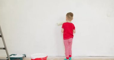 Boya silindiriyle duvar boyayan çocuk. Bir çocuk özenle duvarı beyaza boyar. Yüksek kalite 4k görüntü