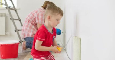 Anne ve oğlu boya silindiri ve fırçayla duvar boyuyor, birlikte tadilatın keyfini çıkarıyorlar. Ailecek vakit geçireceğiz. Kalacak yer ve aile kavramı. Yüksek kalite 4k görüntü