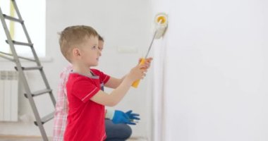 Anne ve oğlu boya silindiri ve fırçayla duvar boyuyor, birlikte tadilatın keyfini çıkarıyorlar. Ailecek vakit geçireceğiz. Kalacak yer ve aile kavramı. Yüksek kalite 4k görüntü